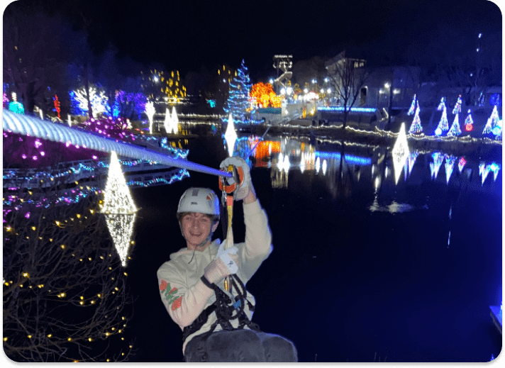 person on zip line with Christmas Town behind him at night