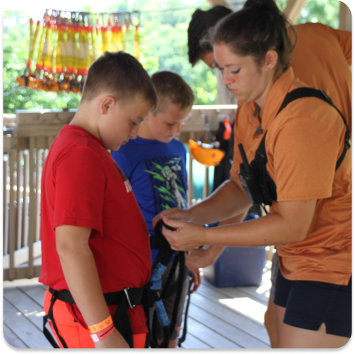 people helping set up kids safety gear before starting a zip line course