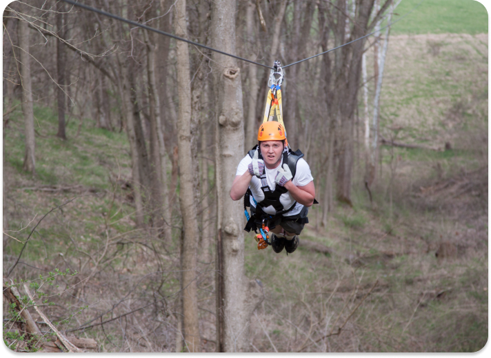 person posing for the camera while on a zipline in Kentucky with trees in the background